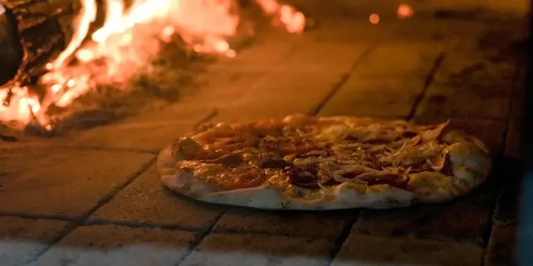 A pepperoni pizza sits on a surface near a blazing fire, illustrating a discussion about whether pizza can cause bad dreams.