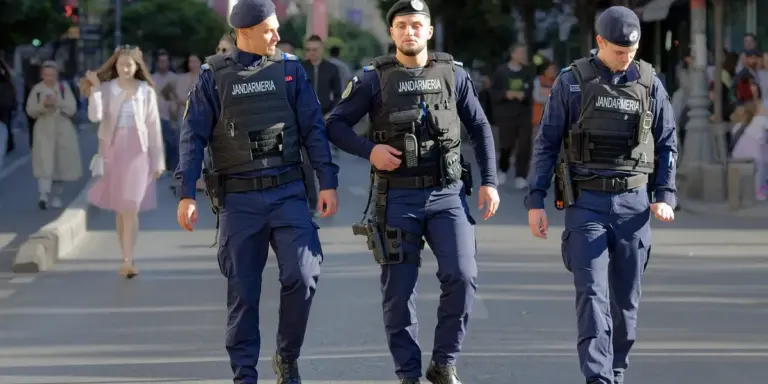 Three police officers in tactical uniforms walking down a city street, with bystanders in the background.