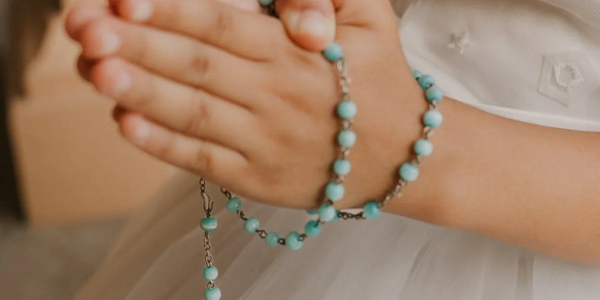 Close-up of hands held in prayer with turquoise beaded rosary draped over wrists