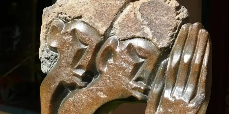 Close-up of weathered stone hands clasped in prayer