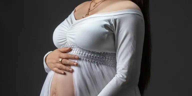 Pregnant woman in a white off-shoulder dress cradling her belly against a dark background.