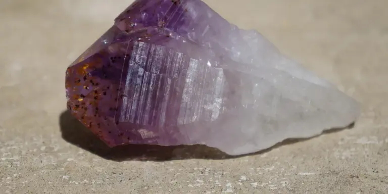 Purple amethyst crystal on a sandy surface, symbolizing the spiritual meaning of the color purple in dreams.