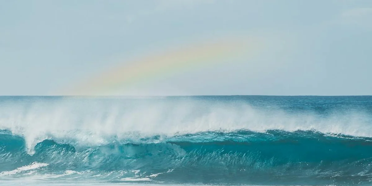 Rainbow arching over a turquoise ocean with curling waves, symbolizing dream symbolism and spiritual meaning.
