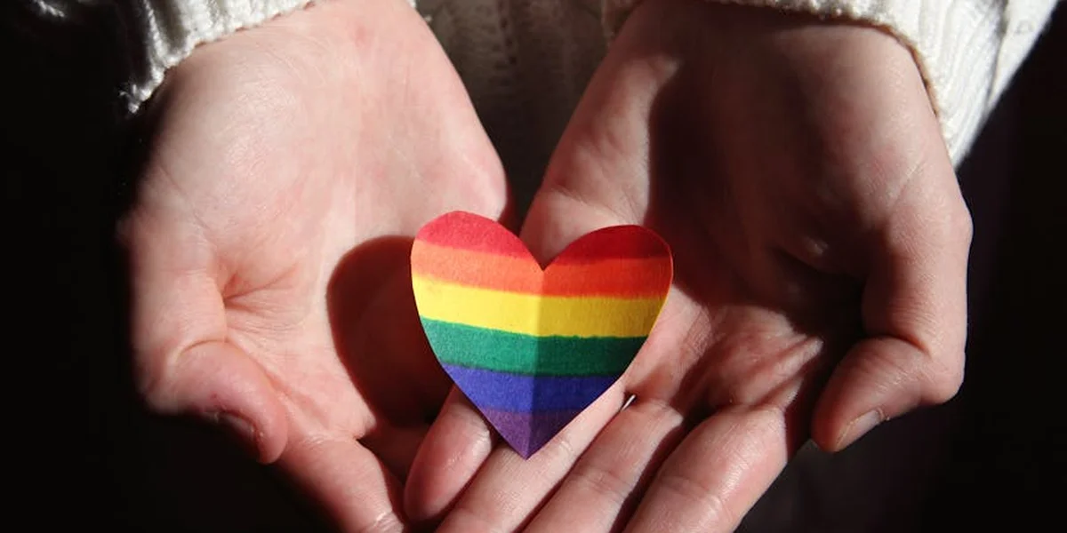 Hands cupping a small rainbow-colored heart against a dark background