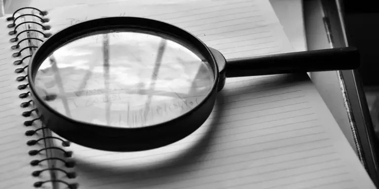 A close-up of a magnifying glass resting on an open spiral notebook, with a pencil nearby, symbolizing careful examination of recurring dreams.