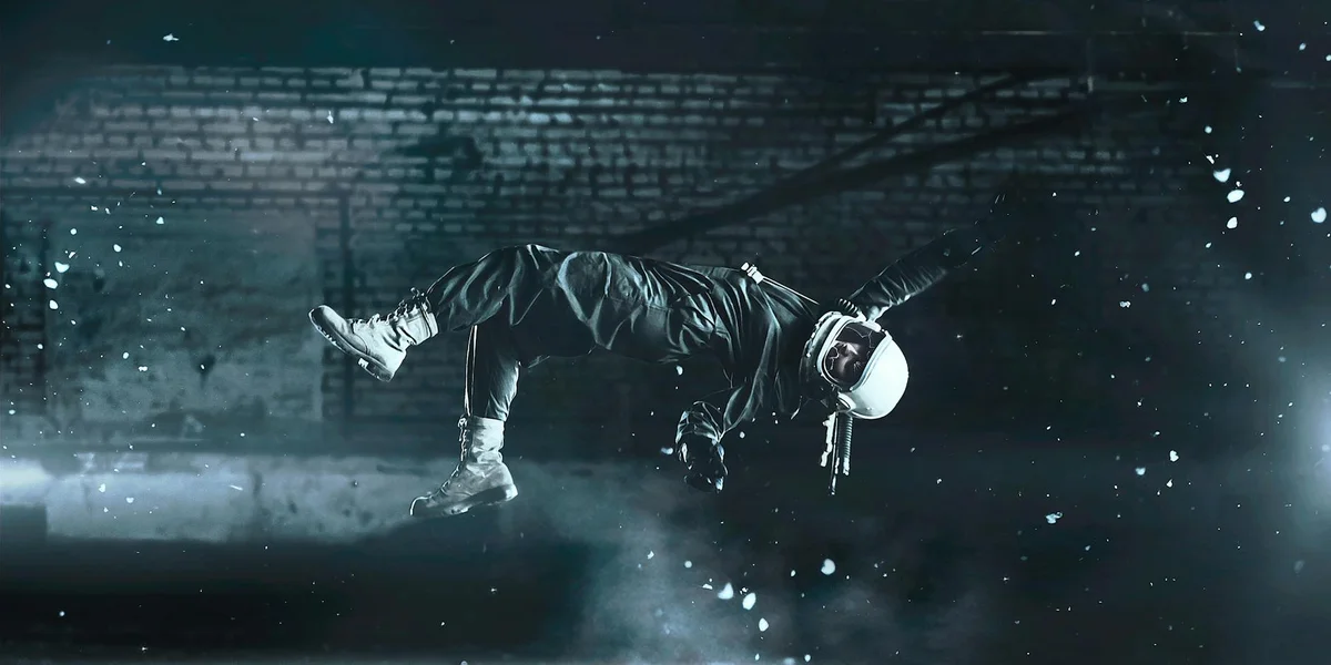 A person in a dark outfit with a white helmet appears to float or leap through a blue, snow-filled night, creating a dreamlike, otherworldly scene.