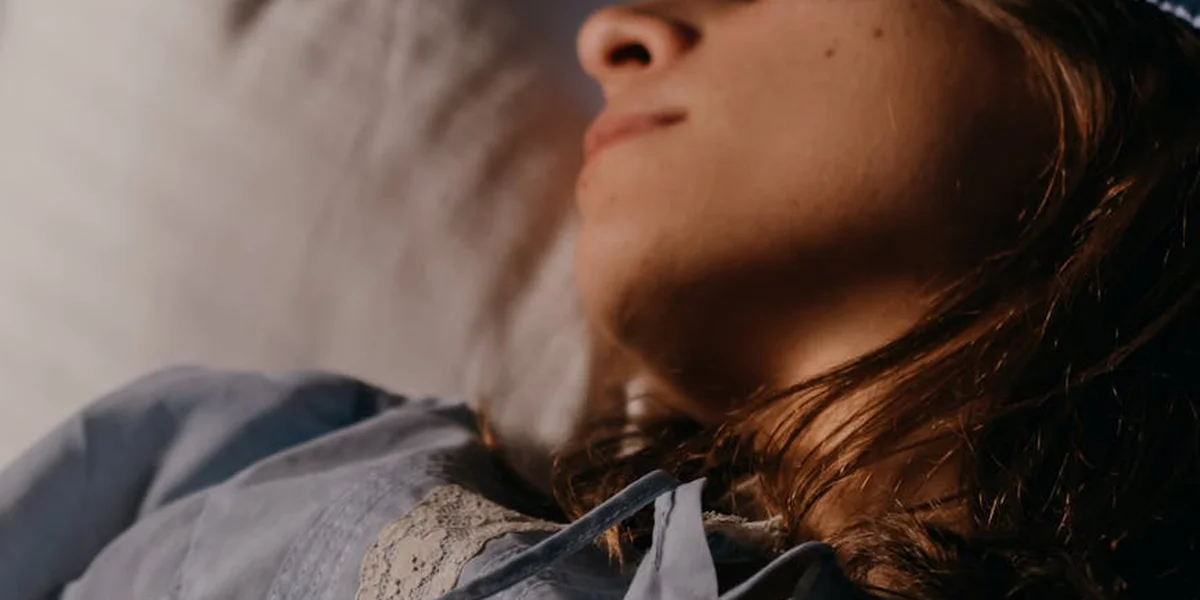 Close-up of a person lying on a bed, head turned to the side, with soft lighting.