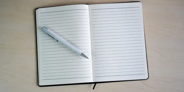 An open, lined notebook with a pen resting on the left page on a light wood surface, ready for journaling about recurring nightmares.