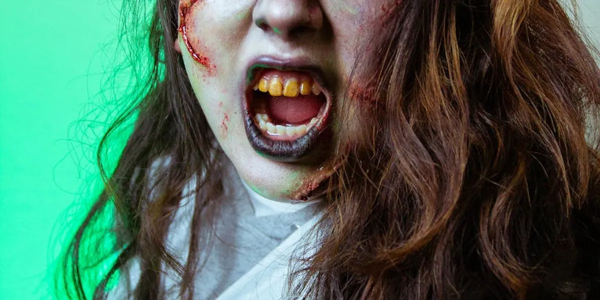 A person with dramatic horror-inspired makeup and an open mouth against a green background, conveying a terrifying recurring nightmare image.