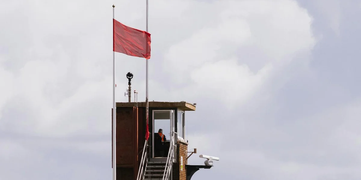 Lifeguard tower with a bright red flag against a cloudy sky.