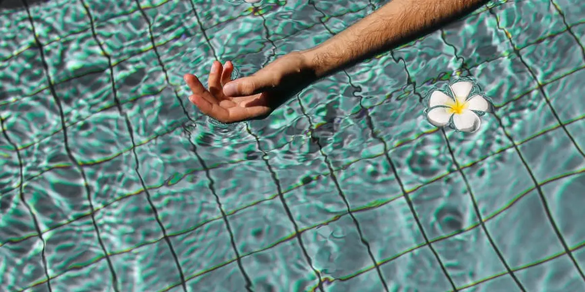 An arm reaches from a swimming pool with turquoise rippling water and a single white flower floating nearby, symbolizing movement and taking action