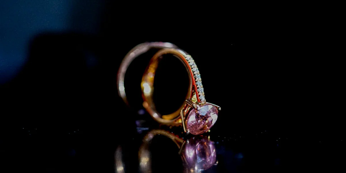 Close-up of a gold ring with a pink gemstone resting on a dark, reflective surface.