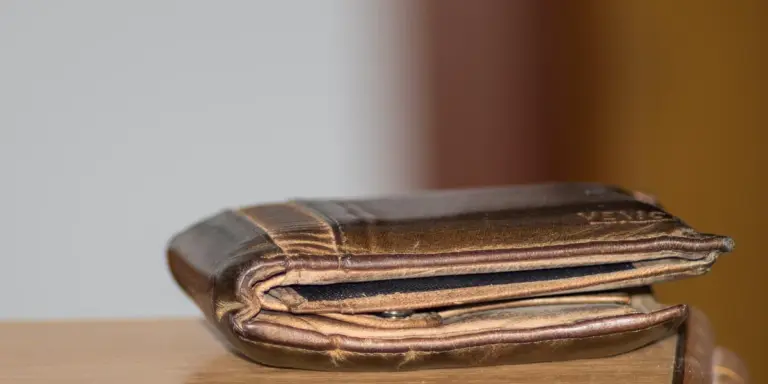 A worn brown leather wallet folded shut on a light surface, suggesting loss and vulnerability.