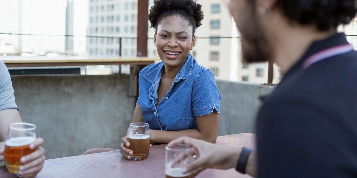 A diverse group of friends on a rooftop terrace, smiling and laughing while holding drinks.