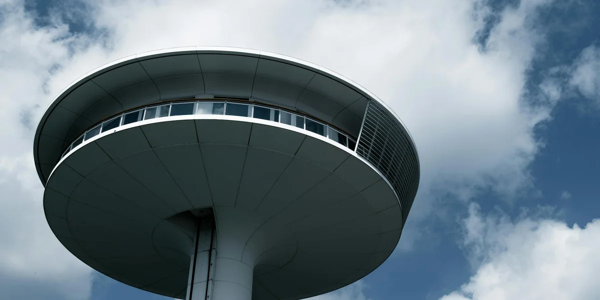 Round, saucer-shaped observation tower on a single pillar against a blue sky with white clouds.