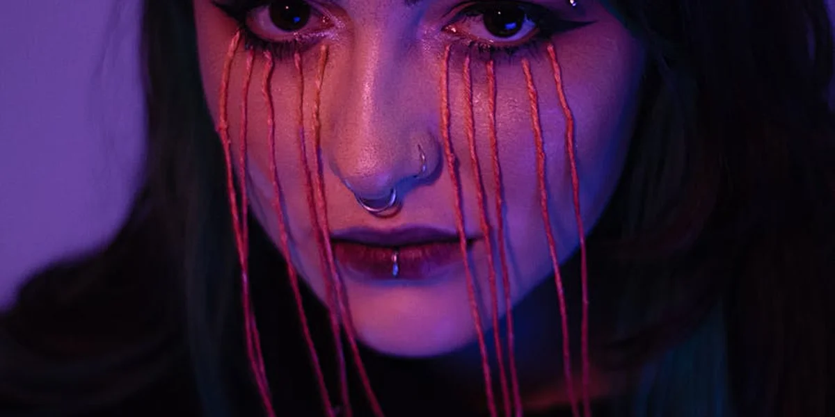 A moody portrait of a person under purple lighting with red tear-like streams running from their eyes, symbolizing nightmares and anxiety dreams.