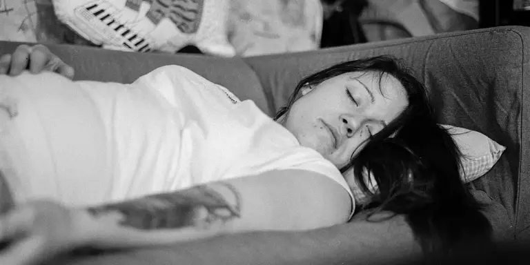 Black-and-white photo of a woman sleeping on a sofa with a pillow under her head.