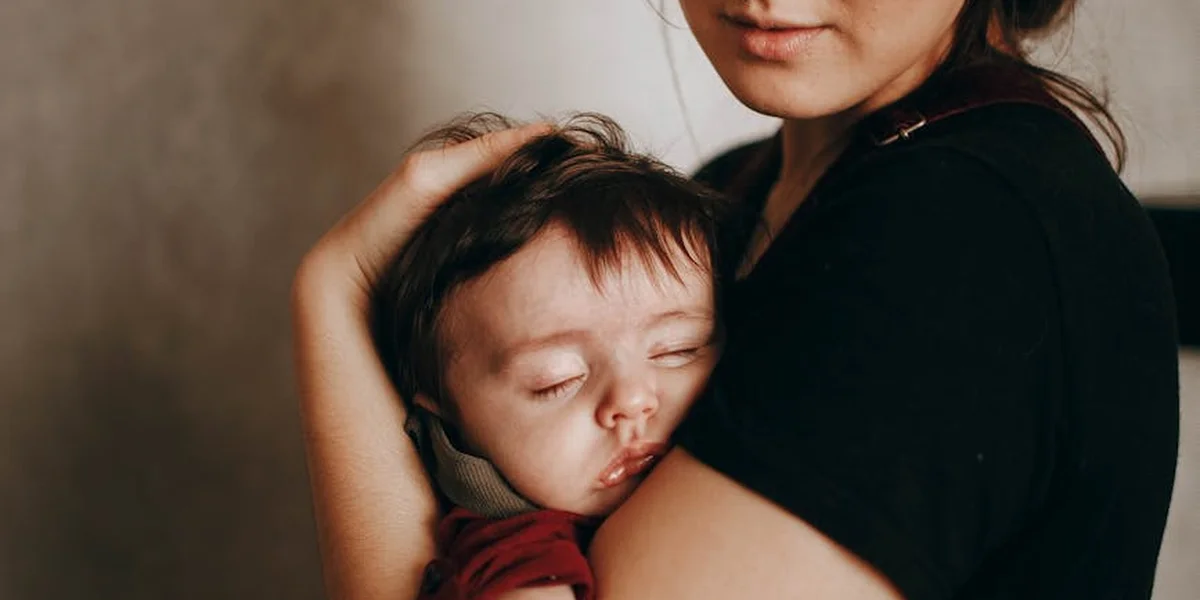A caregiver cradles a sleeping infant in a protective embrace, conveying calm and comfort.
