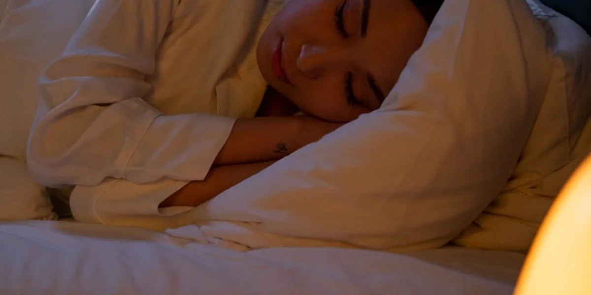 A person sleeps peacefully in white bedding under warm, soft light, illustrating a cozy sleep environment.