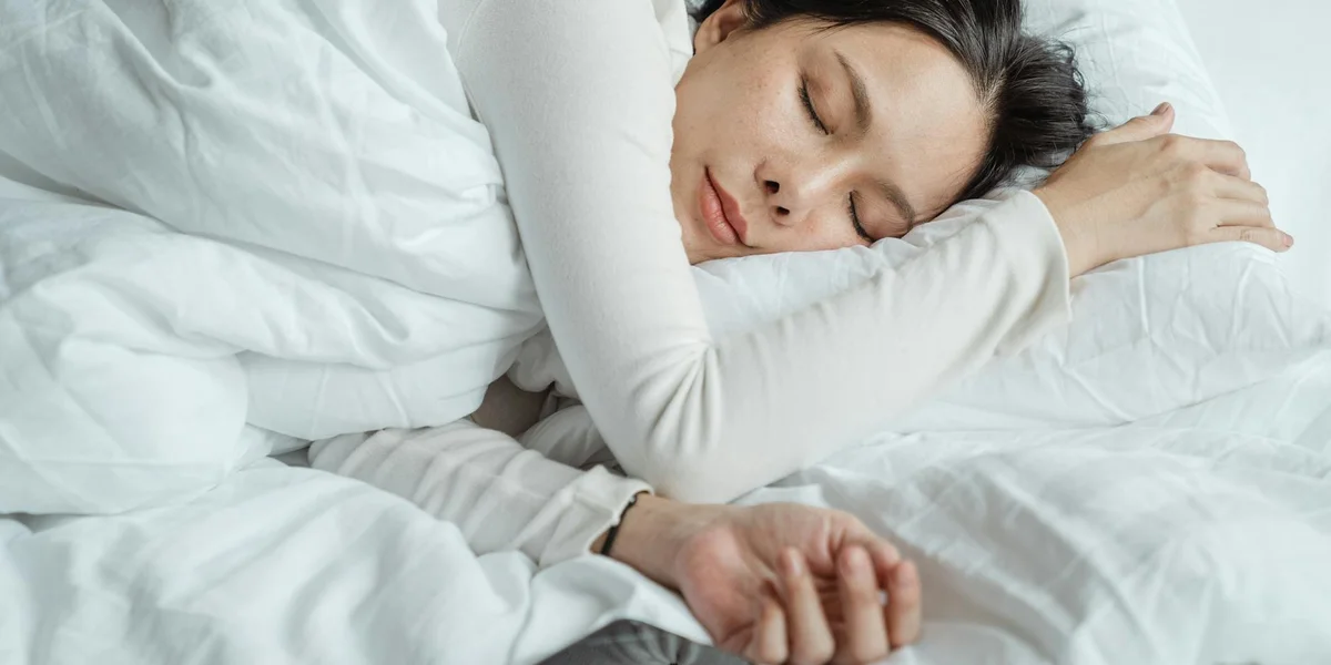 A person sleeping peacefully on white bed linens with eyes closed.
