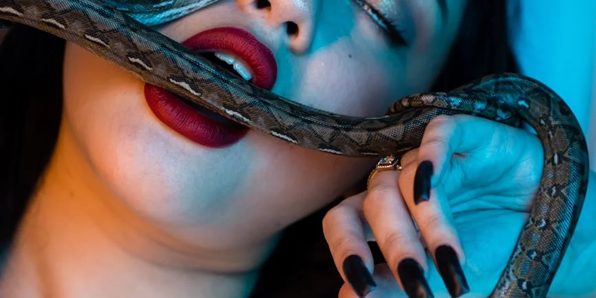 Close-up of a person with bright red lipstick and a snake wrapped around their mouth