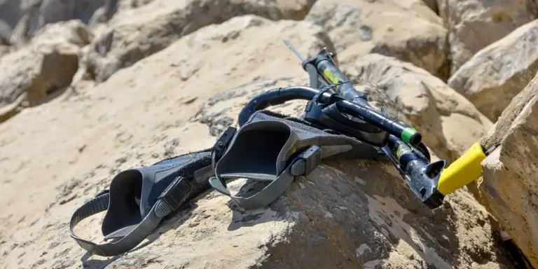 A snorkeling mask and snorkel resting on a rough, rocky surface.