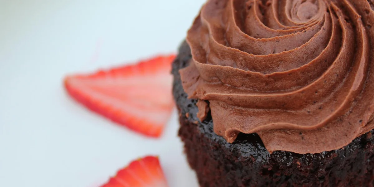 Close-up of a chocolate cupcake with swirled frosting and a sliced strawberry in the background.