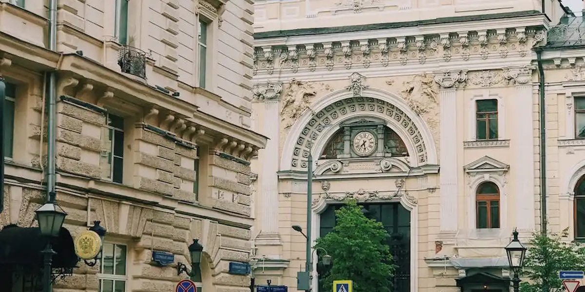 Historic European street with ornate stone facade, arched doorway, and greenery, lampposts along a quiet urban scene.