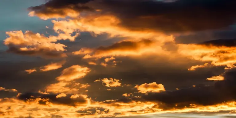 Vivid sunset with orange and gold clouds illuminating a darkening sky.