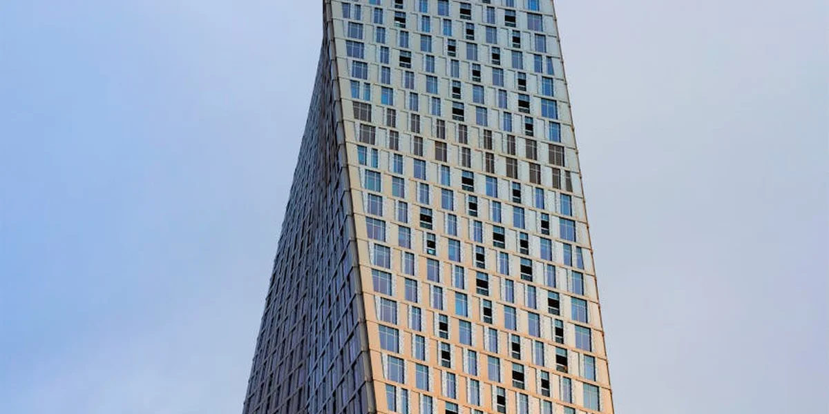 A tall, curved skyscraper with numerous small windows rising against a pale blue sky.