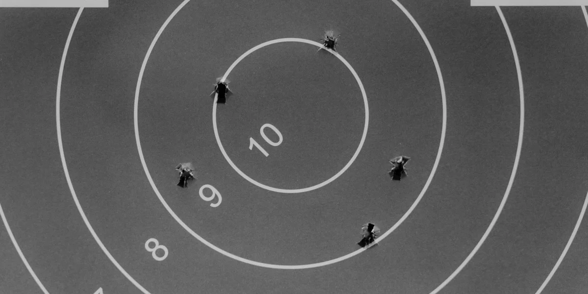 Black-and-white target with multiple bullet holes around the rings.