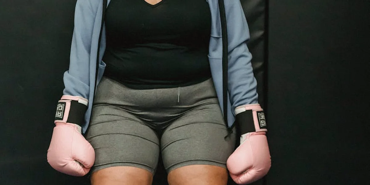 Person wearing a blue jacket and gray shorts with pink boxing gloves, fists raised in a fighting stance.