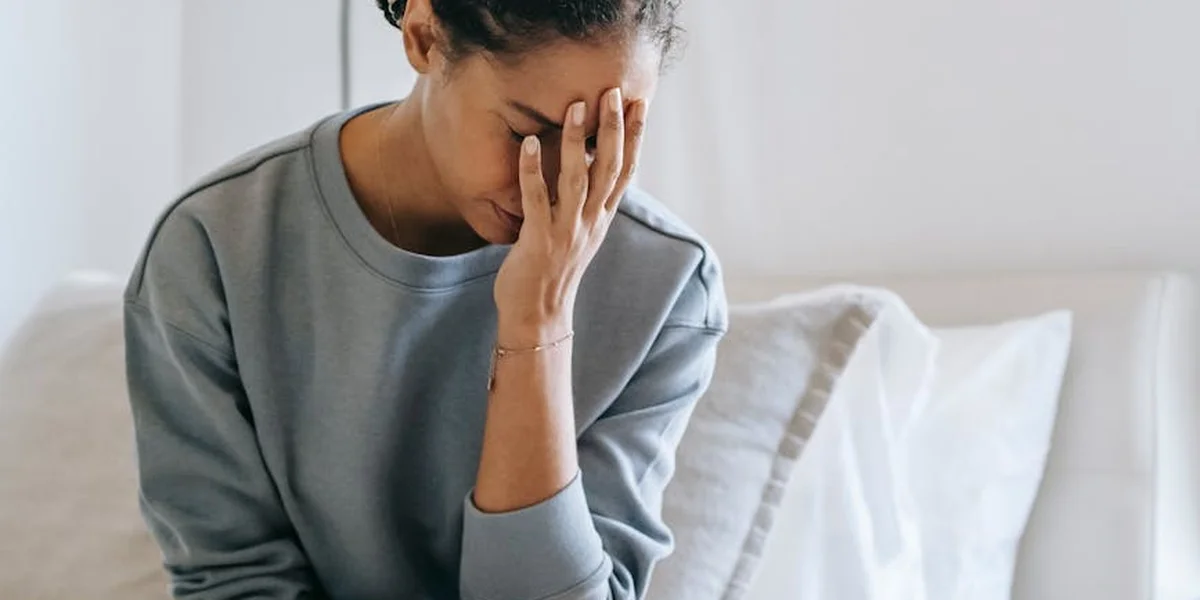 A person sits on a sofa with a pained expression, hand covering their face, conveying distress from nightmares.