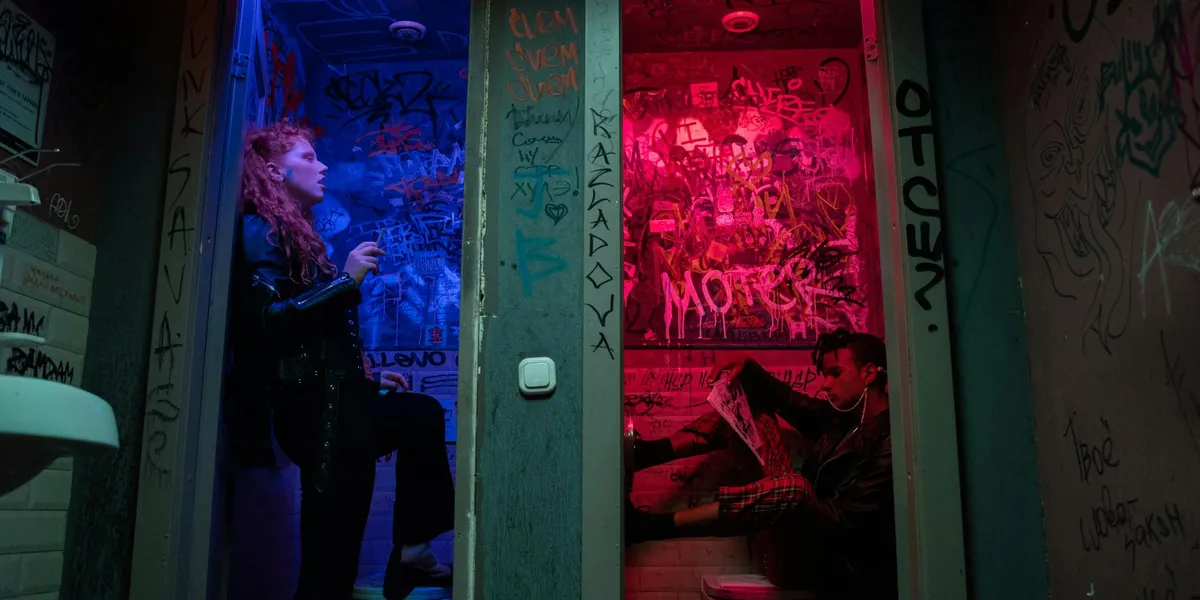 Urban doorway illuminated with blue and pink neon lights, graffiti-covered walls, two people standing in shadows.