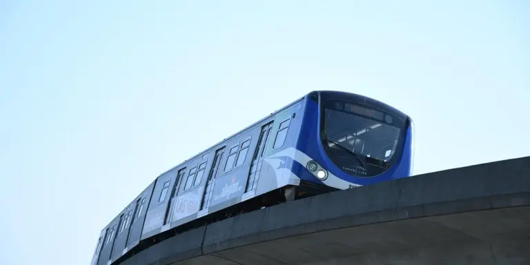 Blue subway train on an elevated curved track against a clear blue sky.