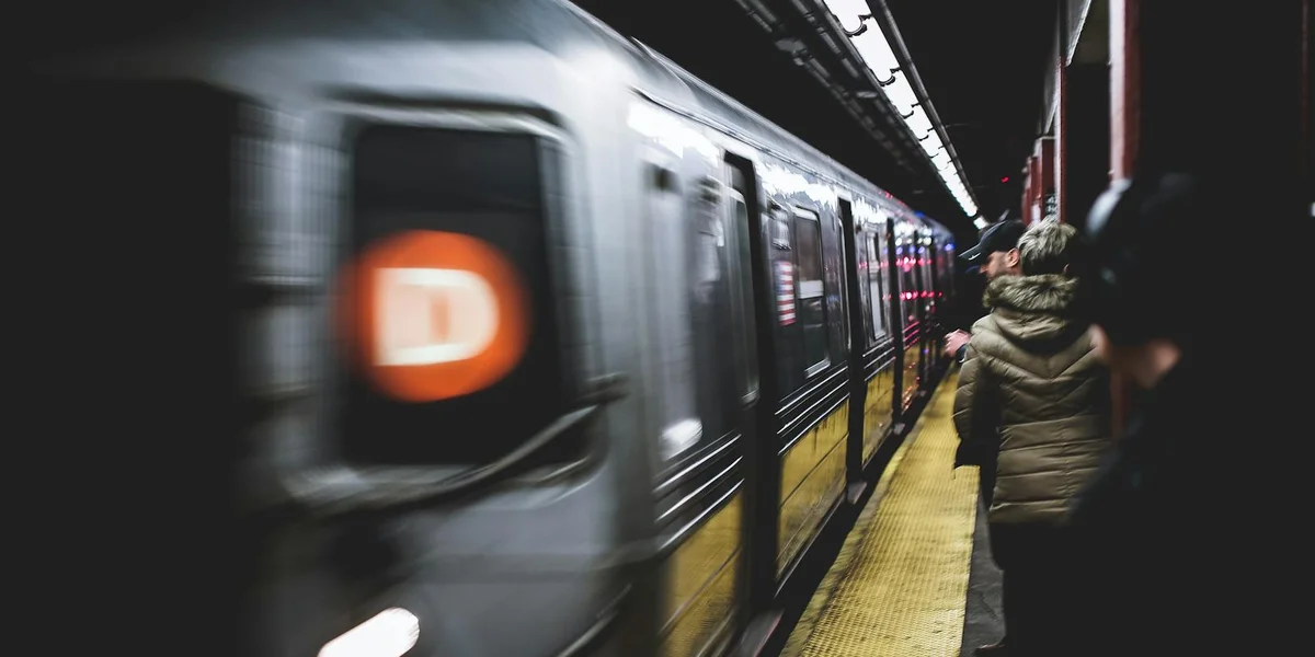 A commuter train at a dimly lit station platform with blurred figures of passengers waiting.