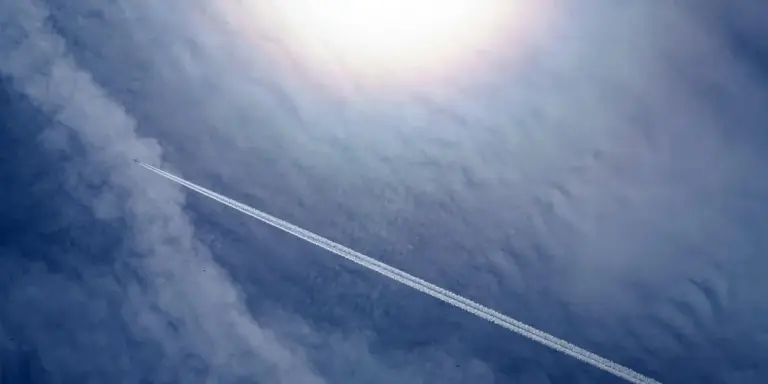 Airplane with a long contrail across a bright blue sky.