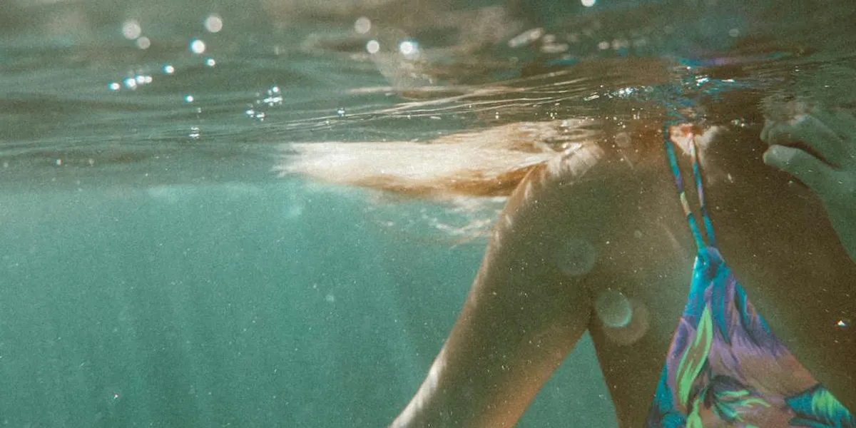 Underwater scene showing a person swimming, light filtering through turquoise water, with colorful swimwear visible near the legs.