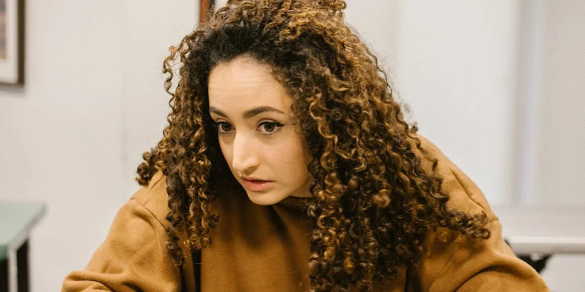 Woman with curly hair wearing a brown top, looking anxious or pensive, symbolizing exam anxiety.