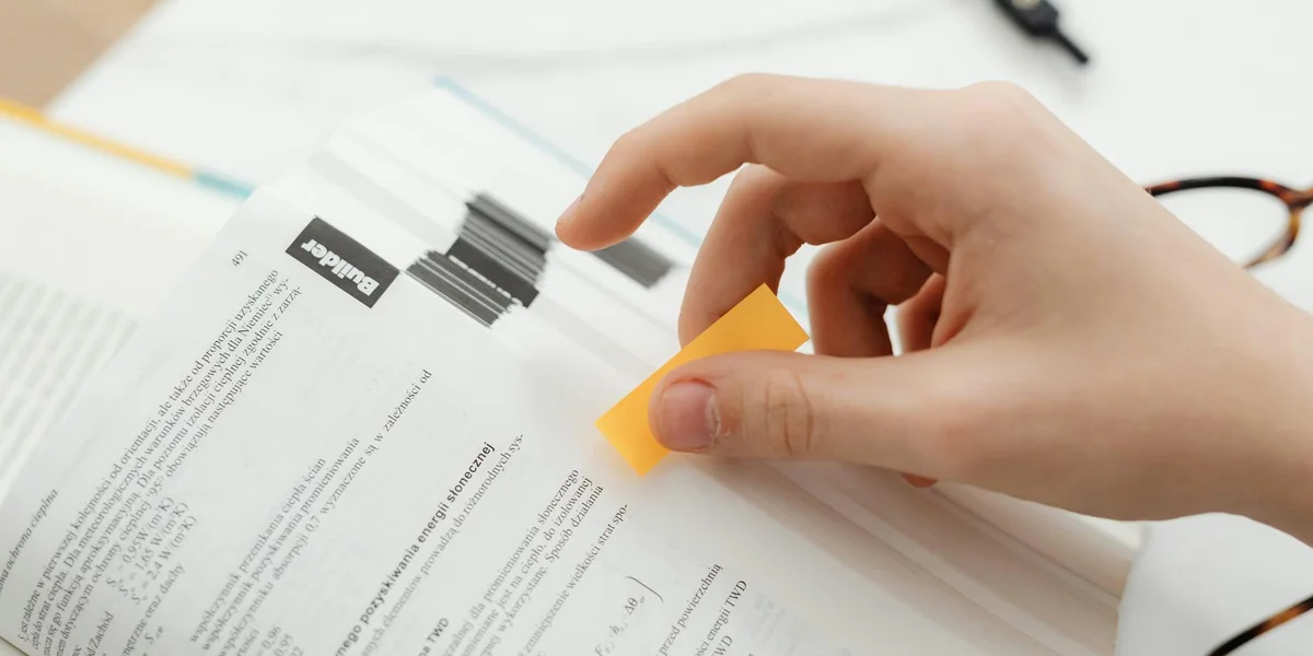 Close-up of a hand peeling a yellow sticky note off a printed test document, with text and a barcode-like area in the background.