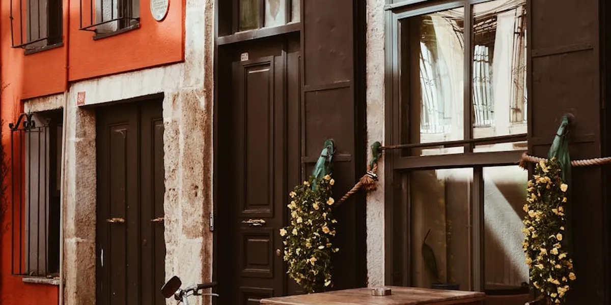 A narrow urban street with colorful facades, dark wooden doors, and windows, accented by hanging plants along the walls.