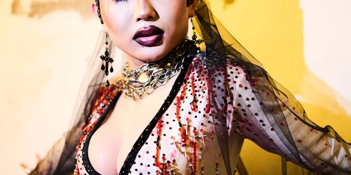 Portrait of a person wearing vampire-inspired makeup with bold red lipstick, ornate jewelry, and a sheer dotted veil.