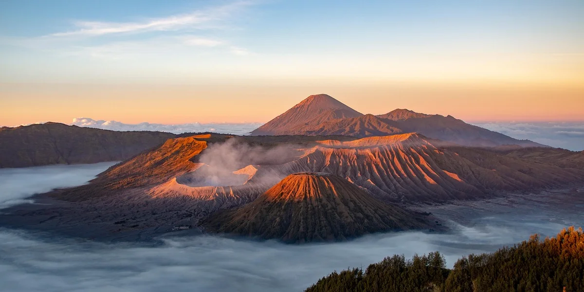 A volcanic landscape at sunrise, with steaming calderas and layered lava ridges, bathed in warm orange light.