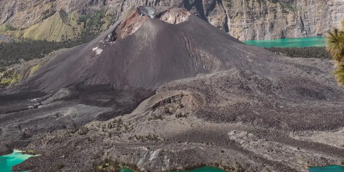 A rugged volcanic landscape with a dark cone and turquoise crater lake, set among rocky terrain.