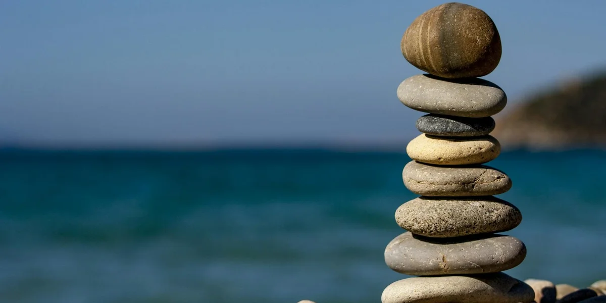 Stacked smooth stones balanced on a beach with the ocean in the background, symbolizing grounding and a personal well.