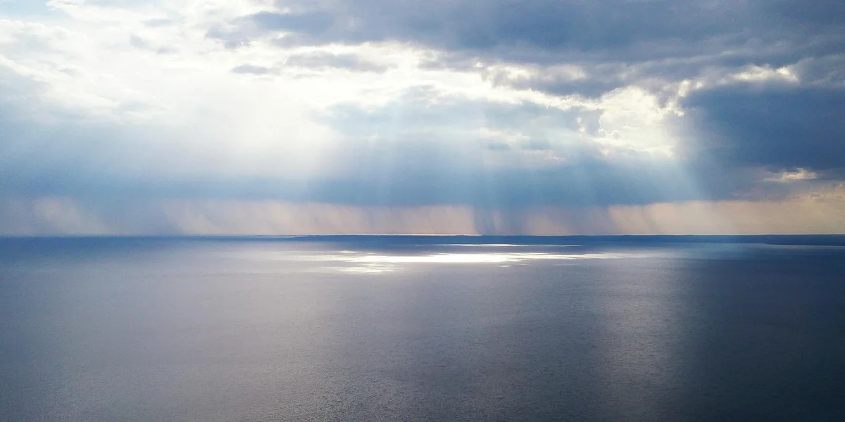 Tranquil sea with a distant horizon and sunlight streaming through clouds, symbolizing divine waters and spiritual renewal.