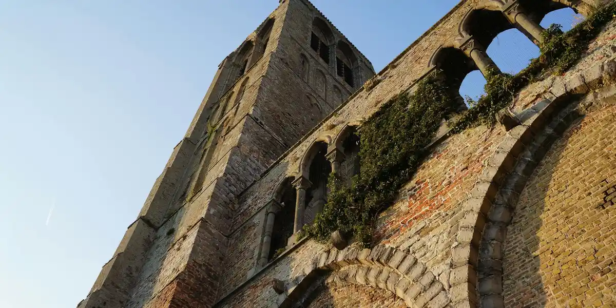 A weathered stone ruin with arched openings and ivy clinging to its walls, set against a clear blue sky.