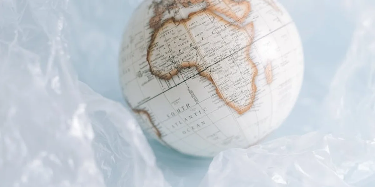 Globe resting on crumpled plastic wrap, suggesting fragility and the precarious state of the world.